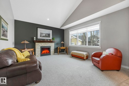 Living space featuring a stone-clad fireplace with a wooden mantel, a large window, and vaulted ceilings - 8112 Summerside Grande Boulevard, Edmonton, AB - Indoor Photo Showing Living Room With Fireplace