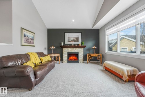 Living room featuring vaulted ceilings, a stone-clad fireplace with a wooden mantel, and a large window providing natural light - 8112 Summerside Grande Boulevard, Edmonton, AB - Indoor Photo Showing Living Room With Fireplace