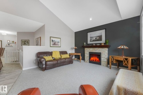 Living area featuring vaulted ceilings, a gray accent wall, and a fireplace with a stone surround - 8112 Summerside Grande Boulevard, Edmonton, AB - Indoor Photo Showing Living Room With Fireplace
