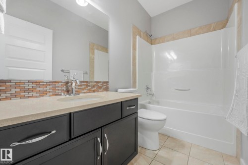 Bathroom featuring a white bathtub with a shower, a vanity with a light-colored countertop, and a mosaic tile backsplash - 8112 Summerside Grande Boulevard, Edmonton, AB - Indoor Photo Showing Bathroom
