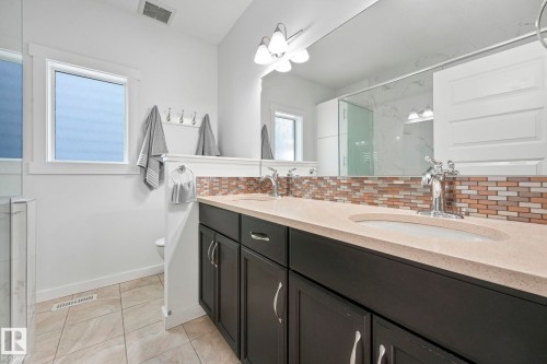 The bathroom features a double vanity with dark cabinetry, light countertops, and a tiled backsplash - 8112 Summerside Grande Boulevard, Edmonton, AB - Indoor Photo Showing Bathroom