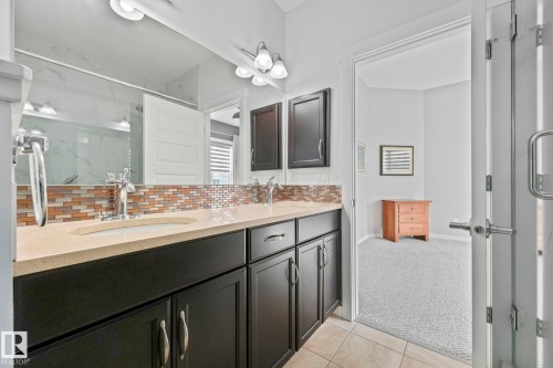 Bathroom with a double vanity featuring a light-colored countertop and dark cabinetry, complemented by a tiled backsplash - 8112 Summerside Grande Boulevard, Edmonton, AB - Indoor Photo Showing Bathroom