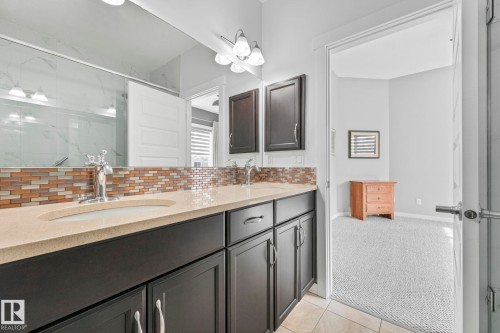 Bathroom featuring a dual vanity with dark cabinetry, light-colored countertops, and a patterned tile backsplash - 8112 Summerside Grande Boulevard, Edmonton, AB - Indoor Photo Showing Bathroom