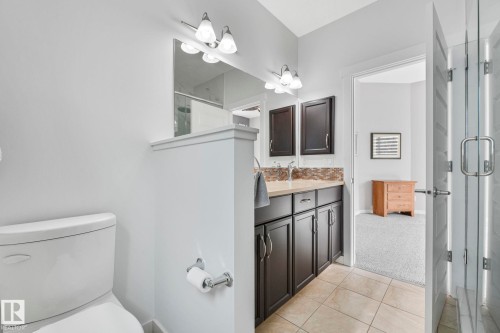 Bathroom featuring a white toilet, tiled flooring, dark wood vanity with a light-colored countertop, and a glass-enclosed shower - 8112 Summerside Grande Boulevard, Edmonton, AB - Indoor Photo Showing Bathroom