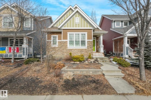 The property features a charming exterior with stone accents and siding, a prominent front porch with white railings, and a distinct lime green front door - 8112 Summerside Grande Boulevard, Edmonton, AB - Outdoor With Facade