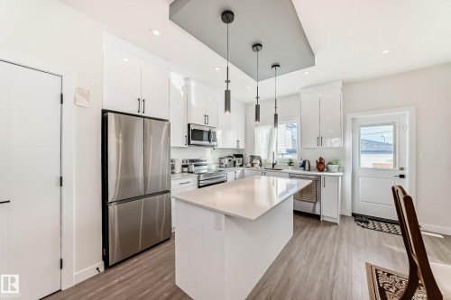 Modern kitchen featuring white cabinetry, stainless steel appliances, a center island with a light-colored countertop, and recessed lighting - 12435 47 Street Nw, Edmonton, AB - Indoor Photo Showing Kitchen With Upgraded Kitchen