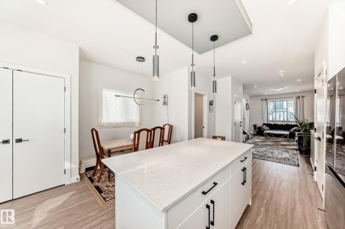 The property features an open concept layout with light-toned flooring throughout, a kitchen island with a light-colored countertop and dark hardware, and modern pendant lighting fixtures - 12435 47 Street Nw, Edmonton, AB - Indoor Photo Showing Kitchen With Upgraded Kitchen