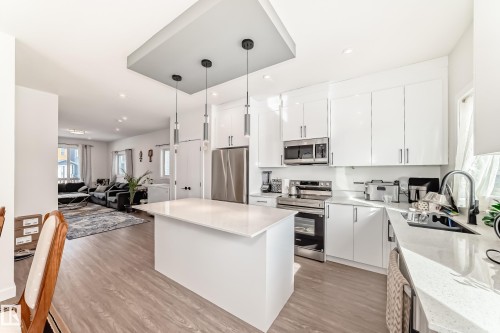 The kitchen features white cabinetry, stainless steel appliances, and a central island with a light-colored countertop. - 12435 47 Street Nw, Edmonton, AB - Indoor Photo Showing Kitchen With Upgraded Kitchen