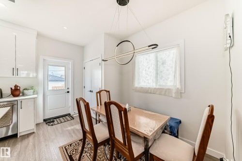 This dining area features light-colored flooring, a window providing natural light, and a modern chandelier - 12435 47 Street Nw, Edmonton, AB - Indoor Photo Showing Dining Room