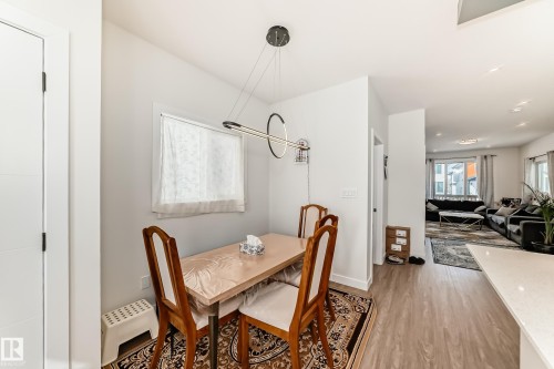 Dining area featuring a modern linear chandelier, a window with natural light, and hardwood style flooring - 12435 47 Street Nw, Edmonton, AB - Indoor Photo Showing Dining Room