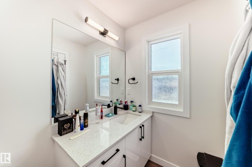 Bathroom vanity with a white countertop and a rectangular sink, complemented by a large mirror and modern lighting fixture - 12435 47 Street Nw, Edmonton, AB - Indoor Photo Showing Bathroom