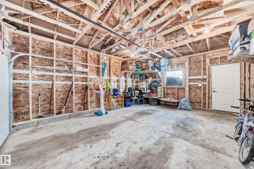 Spacious garage featuring a finished concrete floor, exposed wooden ceiling beams, and a white access door.  There is a concrete back drive area. Back lane is presently not paved. - 12435 47 Street Nw, Edmonton, AB - Indoor Photo Showing Garage