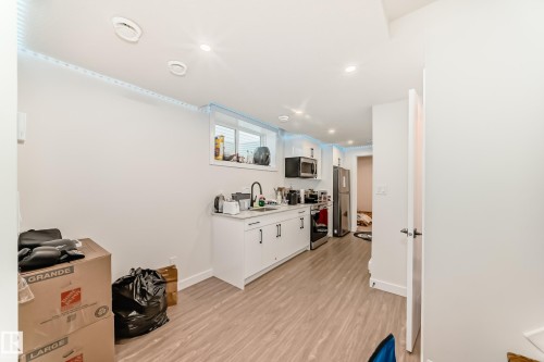 The property features a kitchen area with light-toned flooring, white cabinetry, and stainless steel appliances, Refrigerator., Microwave and electric stove. - 12435 47 Street Nw, Edmonton, AB - Indoor Photo Showing Other Room