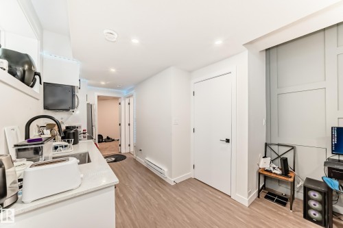 This property features light wood-look flooring, a kitchen area with a sink and white countertops, and white walls throughout - 12435 47 Street Nw, Edmonton, AB - Indoor