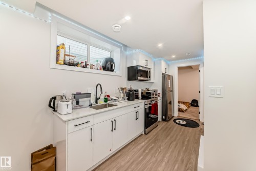 The kitchen features white cabinetry, a stainless steel refrigerator, an oven with a range, and a microwave - 12435 47 Street Nw, Edmonton, AB - Indoor Photo Showing Kitchen