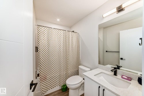 The bathroom features a modern vanity with a white countertop and an integrated sink, a toilet, and a shower area with a patterned shower curtain - 12435 47 Street Nw, Edmonton, AB -  With Deck Patio Veranda With Exterior