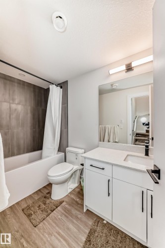 Well-appointed bathroom featuring a tub with dark tile surround, a toilet, a vanity with a white countertop, and a large wall mirror - 12435 47 Street Nw, Edmonton, AB - Indoor Photo Showing Bathroom