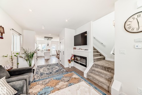 Inviting living area featuring Laminate flooring, an electric fireplace, and a carpeted staircase to the upper level. - 12435 47 Street Nw, Edmonton, AB - Indoor Photo Showing Living Room With Fireplace