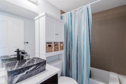 Bathroom featuring a rectangular vessel sink with a marble-like finish, a white vanity with open shelving, and a bathtub with tiled walls - 