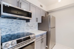 Kitchen featuring stainless steel appliances, light grey cabinetry with black hardware, white countertops, and a subway tile backsplash - 