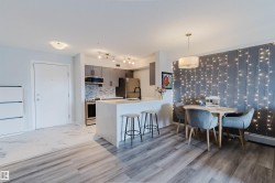 Open concept living area featuring wood-look flooring and a kitchen with stainless steel appliances, grey cabinetry, and a white marble-look island - 