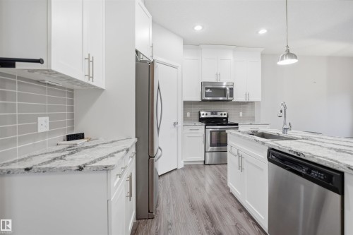 The kitchen features white cabinetry, granite countertops, a tile backsplash, and stainless steel appliances, including a refrigerator, microwave, oven, and dishwasher - 8424 Cushing Court, Edmonton, AB - Indoor Photo Showing Kitchen With Upgraded Kitchen