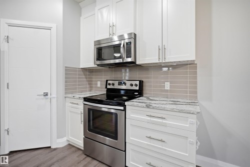 The kitchen features white cabinetry, stainless steel appliances including a range and microwave, and light-colored countertops - 8424 Cushing Court, Edmonton, AB - Indoor Photo Showing Kitchen With Upgraded Kitchen