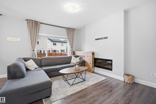 The living area features wood-look flooring, a modern fireplace, and a sliding glass door leading to the outdoor space - 8424 Cushing Court, Edmonton, AB - Indoor Photo Showing Living Room With Fireplace