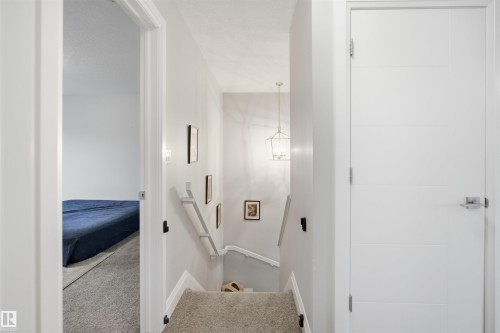 Hallway featuring light gray walls, a modern pendant light fixture, and a carpeted staircase with white railings - 8424 Cushing Court, Edmonton, AB - Indoor Photo Showing Other Room