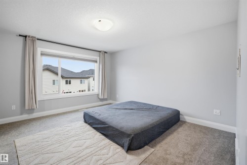 This room features light grey walls, grey carpet flooring, and a large window with neutral-toned curtains - 8424 Cushing Court, Edmonton, AB - Indoor Photo Showing Bedroom