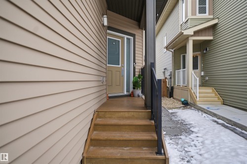 The property entrance features a wooden staircase with a dark railing leading to a light brown door with a window insert, set against beige siding - 8424 Cushing Court, Edmonton, AB - Outdoor With Exterior