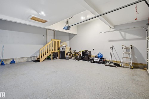 The property features a spacious garage with a light grey floor, an automatic garage door opener, and a wooden staircase - 8424 Cushing Court, Edmonton, AB - Indoor Photo Showing Garage