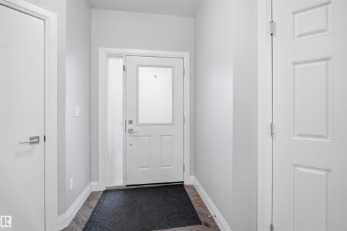 The property features a front entry with a white door, a sidelight, and wood-look flooring - 8424 Cushing Court, Edmonton, AB - Indoor Photo Showing Other Room