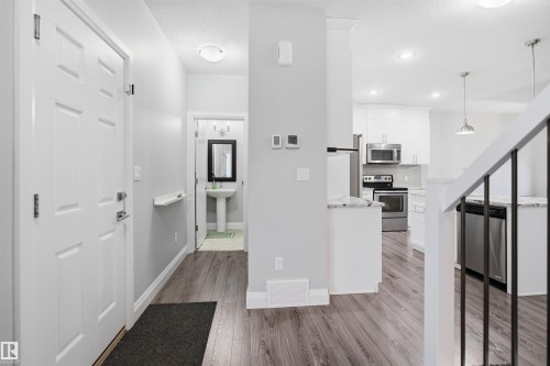 The property features a white paneled door, wood-look flooring, and a kitchen with white cabinetry and stainless steel appliances - 8424 Cushing Court, Edmonton, AB - Indoor