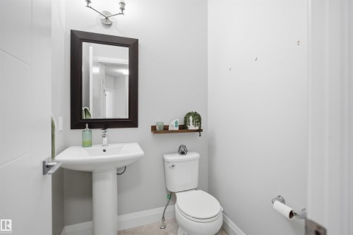 Bathroom with a pedestal sink, a toilet, a mirror with a dark frame, and a wall-mounted light fixture - 8424 Cushing Court, Edmonton, AB - Indoor Photo Showing Bathroom