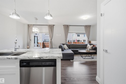 Open concept living area featuring a kitchen island with a double sink and stainless steel dishwasher, hardwood flooring, and neutral wall colors - 8424 Cushing Court, Edmonton, AB - Indoor