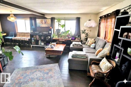 Living area featuring dark wood floors, large windows with dark curtains, and a decorative chandelier - 11 Willow Park Estates, Leduc, AB - Indoor Photo Showing Living Room