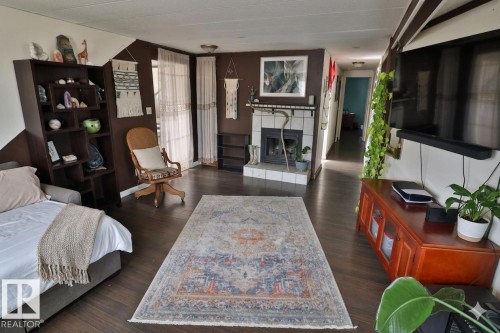 Spacious living area featuring dark wood flooring, a fireplace with a tiled surround, and large windows with sheer curtains - 11 Willow Park Estates, Leduc, AB - Indoor With Fireplace