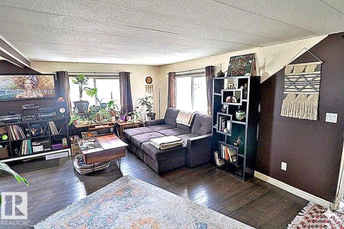 The living area features dark wood-style flooring, a large window with dark curtains, and a textured white ceiling - 11 Willow Park Estates, Leduc, AB - Indoor