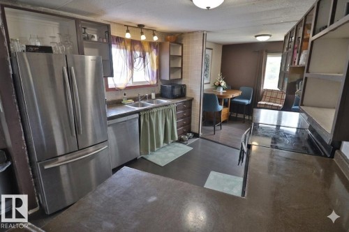 The kitchen features stainless steel appliances, including a refrigerator and dishwasher, with a double basin sink and track lighting - 11 Willow Park Estates, Leduc, AB - Indoor Photo Showing Kitchen With Double Sink