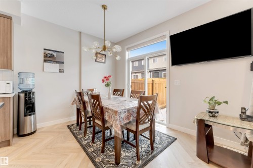 The dining area features light-toned herringbone flooring, a modern chandelier, and sliding glass doors that open to a fenced outdoor area - 6404 27 Avenue, Edmonton, AB - Indoor Photo Showing Dining Room