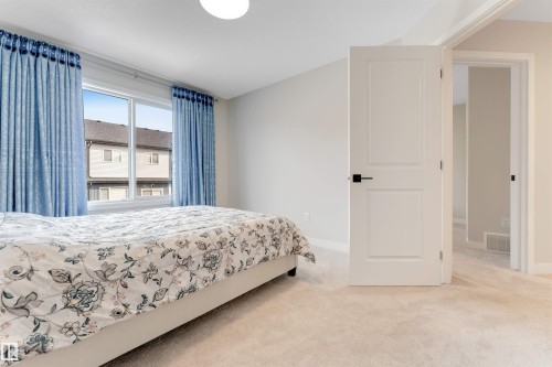 This room features carpeted flooring, light-colored walls, a window with blue curtains, and a white door with black hardware - 6404 27 Avenue, Edmonton, AB - Indoor Photo Showing Bedroom