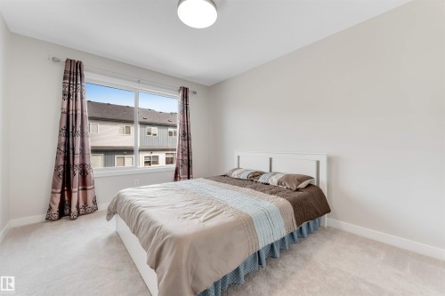 This bedroom features light-colored walls, a large window with patterned curtains, and a light-colored carpet - 6404 27 Avenue, Edmonton, AB - Indoor Photo Showing Bedroom