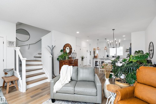 This bright interior features light-colored flooring, a staircase with white risers and handrails, and a kitchen area with pendant lighting - 20 Hemingway Crescent, Spruce Grove, AB - Indoor Photo Showing Living Room