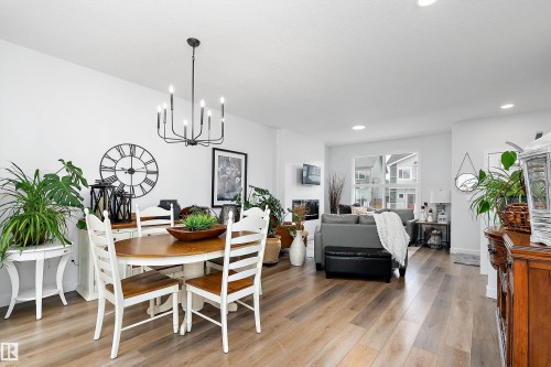 This open-concept living area features light wood flooring throughout, a modern chandelier, and a large window providing views of the exterior - 20 Hemingway Crescent, Spruce Grove, AB - Indoor Photo Showing Dining Room
