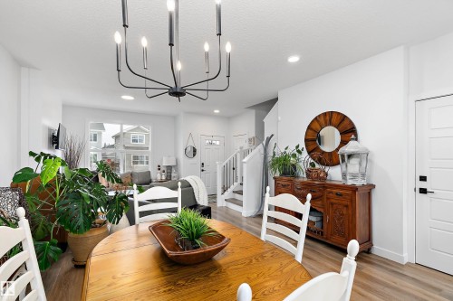 Dining area featuring a modern black chandelier, hardwood style flooring, and an open concept view to the living area - 20 Hemingway Crescent, Spruce Grove, AB - Indoor Photo Showing Dining Room
