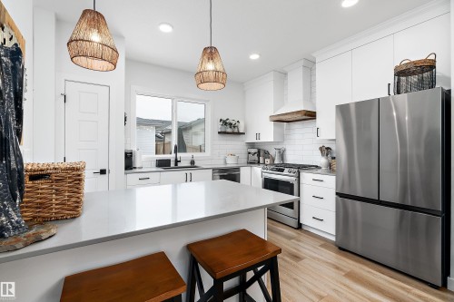 The kitchen features a spacious island with a light-colored countertop, white cabinetry with dark hardware, and stainless steel appliances including a refrigerator and range - 20 Hemingway Crescent, Spruce Grove, AB - Indoor Photo Showing Kitchen With Upgraded Kitchen