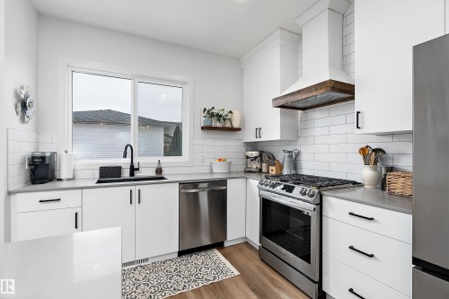 Well-appointed kitchen featuring white cabinetry, a white subway tile backsplash, stainless steel appliances, and a wood-accented range hood - 20 Hemingway Crescent, Spruce Grove, AB - Indoor Photo Showing Kitchen With Upgraded Kitchen