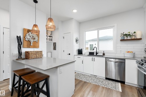 The kitchen features light wood flooring, white cabinetry, a kitchen island with a light-colored countertop, and a stainless steel dishwasher - 20 Hemingway Crescent, Spruce Grove, AB - Indoor Photo Showing Kitchen With Upgraded Kitchen