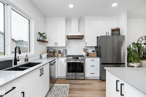 The kitchen features white cabinetry, stainless steel appliances, a double sink, and light-colored countertops - 20 Hemingway Crescent, Spruce Grove, AB - Indoor Photo Showing Kitchen With Double Sink With Upgraded Kitchen